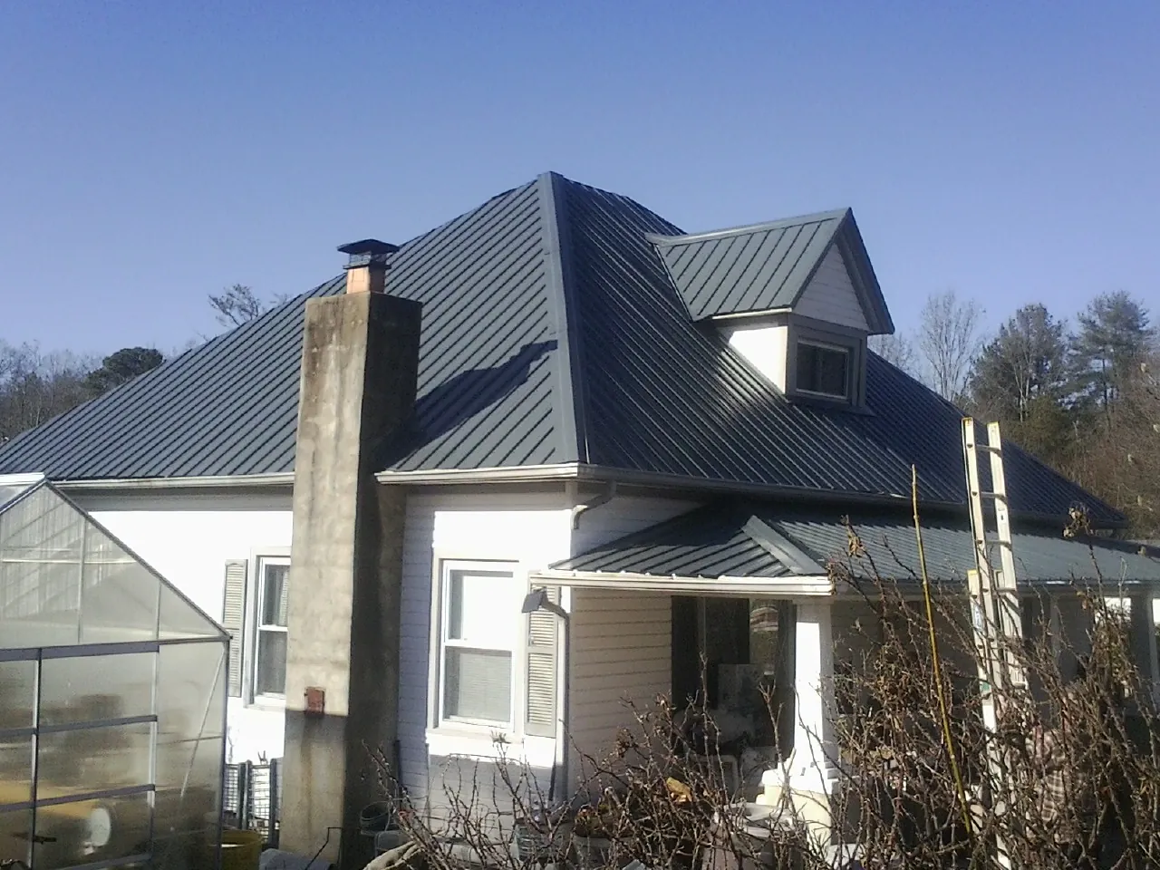 Dark blue standing seam metal roof on a white farmhouse with dormer — Slate & Tile Roof Repair by Roofing Brothers in Pipersville
