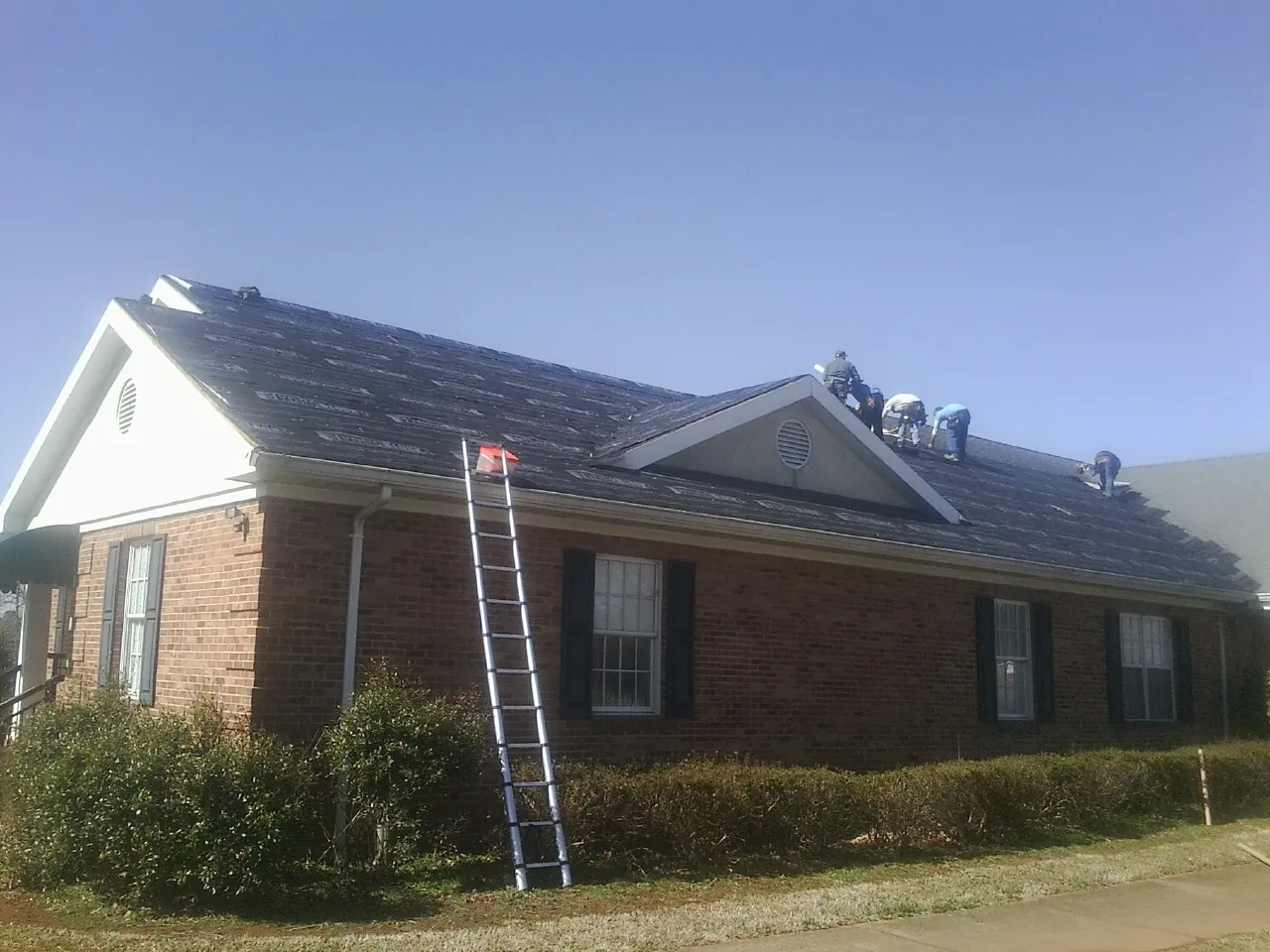 Crew tearing shingles off a brick ranch roof with a ladder set — Metal Roof Repair work by our crew in Pipersville