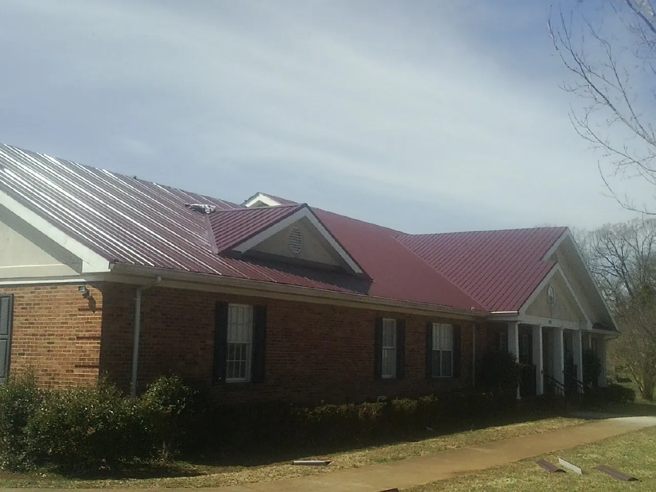 Red metal roof with gabled entries on a long brick building, from a Hail Damage Roof Repair job in Pipersville