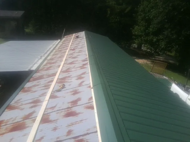 Old rusted panels beside newly installed green metal roofing — Wind Damage Roof Repair by Roofing Brothers in Pipersville
