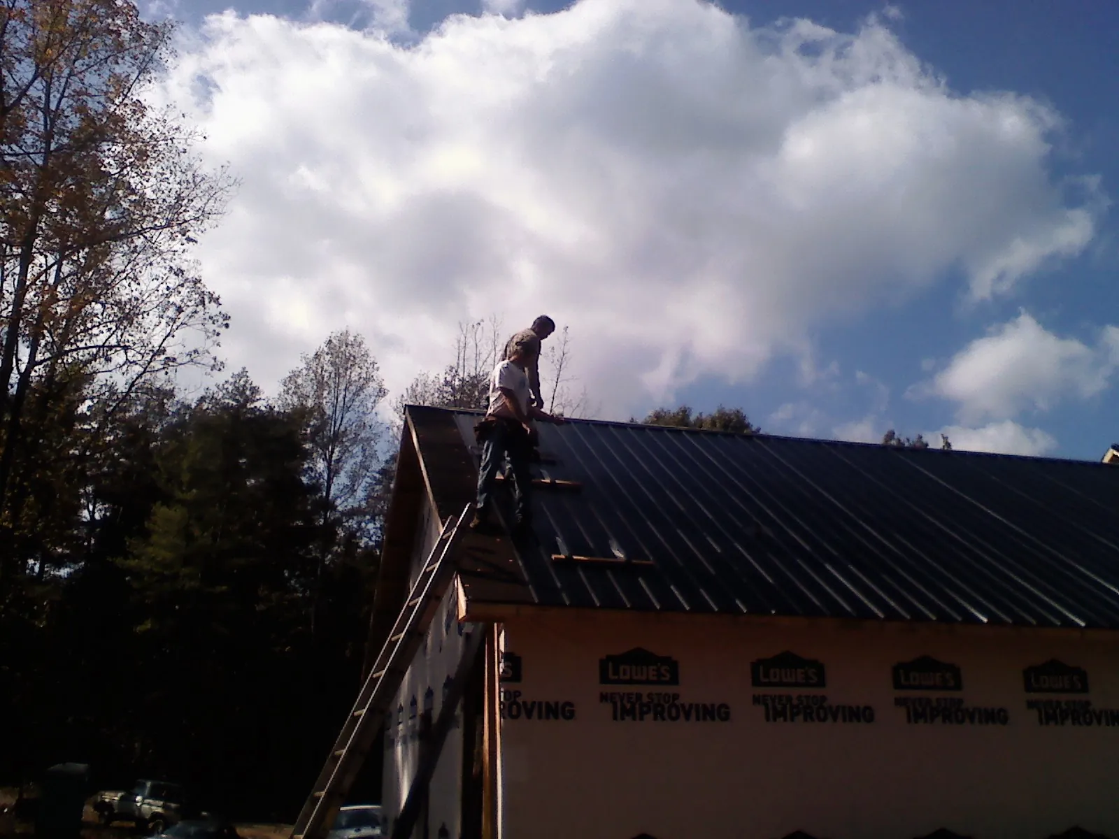 Roofer fastening dark metal panels high against a cloudy sky, from a Roof Inspection job in Pipersville