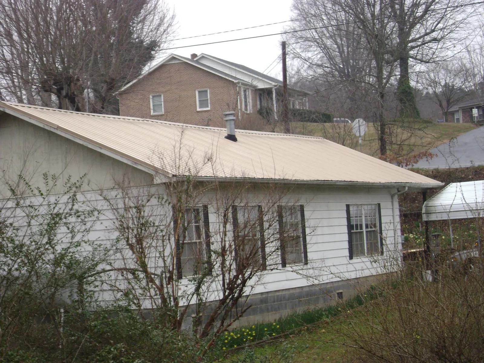 Tan metal roof on a white sided house set into a hillside — Commercial Roofing by Roofing Brothers in Pipersville
